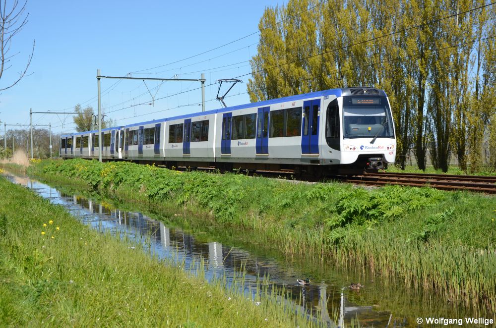 Die Metrolinie E, deren Fahrzeuge ebenfalls in RandstadRail-Farbgebung lackiert sind, verbindet Den Haag und Rotterdam. Die Züge sind sowohl mit Dach- als auch mit Seitenstromabnehmern ausgerüstet. Am 01.05.2016 ist Wagen 5518 zwischen den Stationen Nootdorp und Pijnacker Centrum unterwegs nach Rotterdam.
