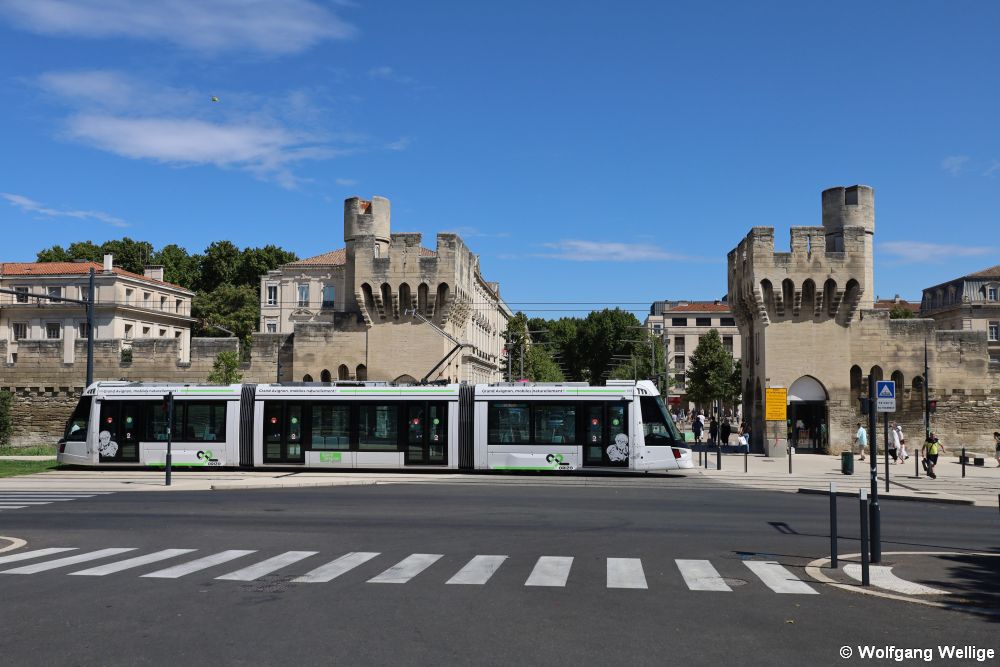 Die Fahrzeuge des Typs Citadis Compact X05 der Tram Avignon sind nur 24 Meter lang. Am 3. August 2020 passiert Wagen 105 die mit stattlichen Türmen versehene Zufahrt zur Altstadt kurz vor der Haltestelle Gare Centre.