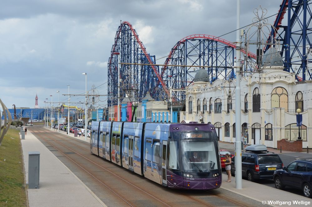 Der mit einer Werbebeklebung versehene Wagen 016 bremst langsam ab, denn er erreicht gleich die Haltestelle Burlington Road West. Deutlich stärkeren Fliehkräften werden die Fahrgäste der hier parallel verlaufenden Achterbahn 'The Big One' des Vergnügungsparks 'Blackpool Pleasure Beach' ausgesetzt.