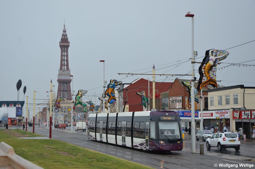 Im Stadtzentrum von Blackpool hat Wagen 012 gerade das Wahrzeichen von Blackpool, den 158 Meter hohen Blackpool Tower, der dem Pariser Eiffelturm nachempfunden und ebenfalls bereits über 100 Jahre alt ist, passiert und fährt nun auf die Haltestelle Manchester Square zu. (05.07.2015)