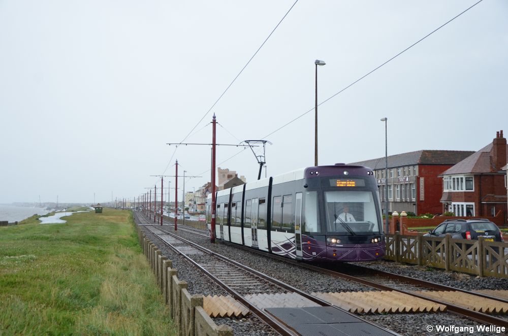 Während eines kräftigen Regenschauers ist Wagen 009 am 05.07.2015 auf dem als Überlandstraßenbahn angelegten Abschnitt nördlich von Blackpool unterwegs, aufgenommen kurz vor der Station Sandhurst Avenue. Die dreieckig geschnittenen Holzbohlen verhindern wie bei vielen britischen Eisenbahnstrecken wirkungsvoll ein Betreten des Gleiskörpers durch Fußgänger.