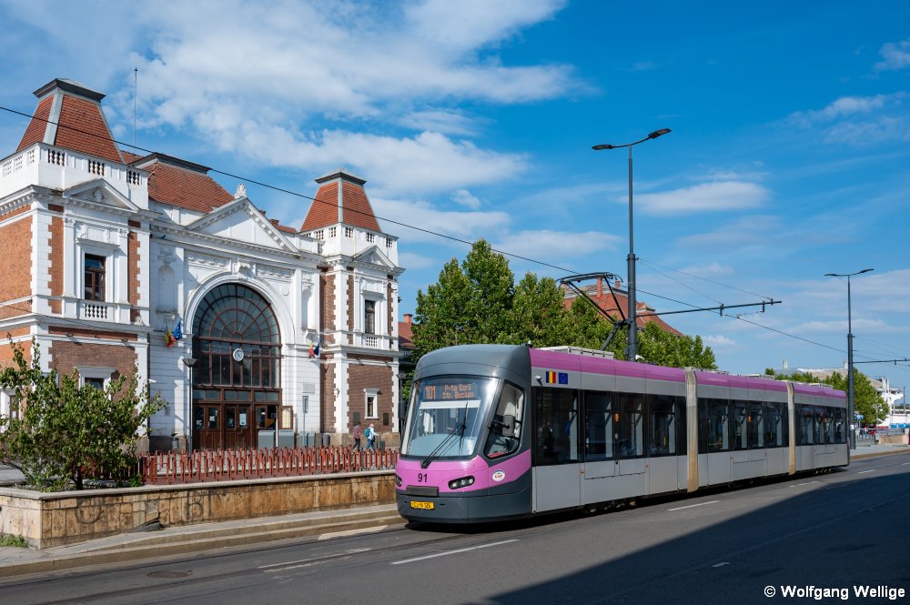 Im Jahre 2021 wurden alle Hochflurfahrzeuge in Cluj-Napoca durch Niederflurfahrzeuge des Typs Astra Imperio ersetzt. Am 7.9.2025 verlässt Wagen 91 gerade die Haltestelle Piața Gării Nord vor dem schön restaurierten Bahnhofsgebäude.