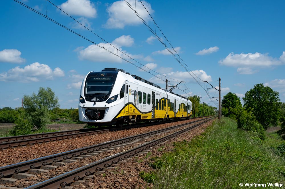 Der im 'Wellendesign' der Niederschlesische Eisenbahnen (Koleje Dolnośląskie) gestaltete, von Newag gebaute 'Impuls 2'-Triebwagen ist am 20.05.2025 als Zug KD 69914 von Trzebnica bei Wrocław Sołtysowice unterwegs nach Wrocław Głowny (Breslau Hbf).